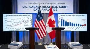 A presentation stage with US and Canadian flags between screens displaying bilateral tariff data analytics.